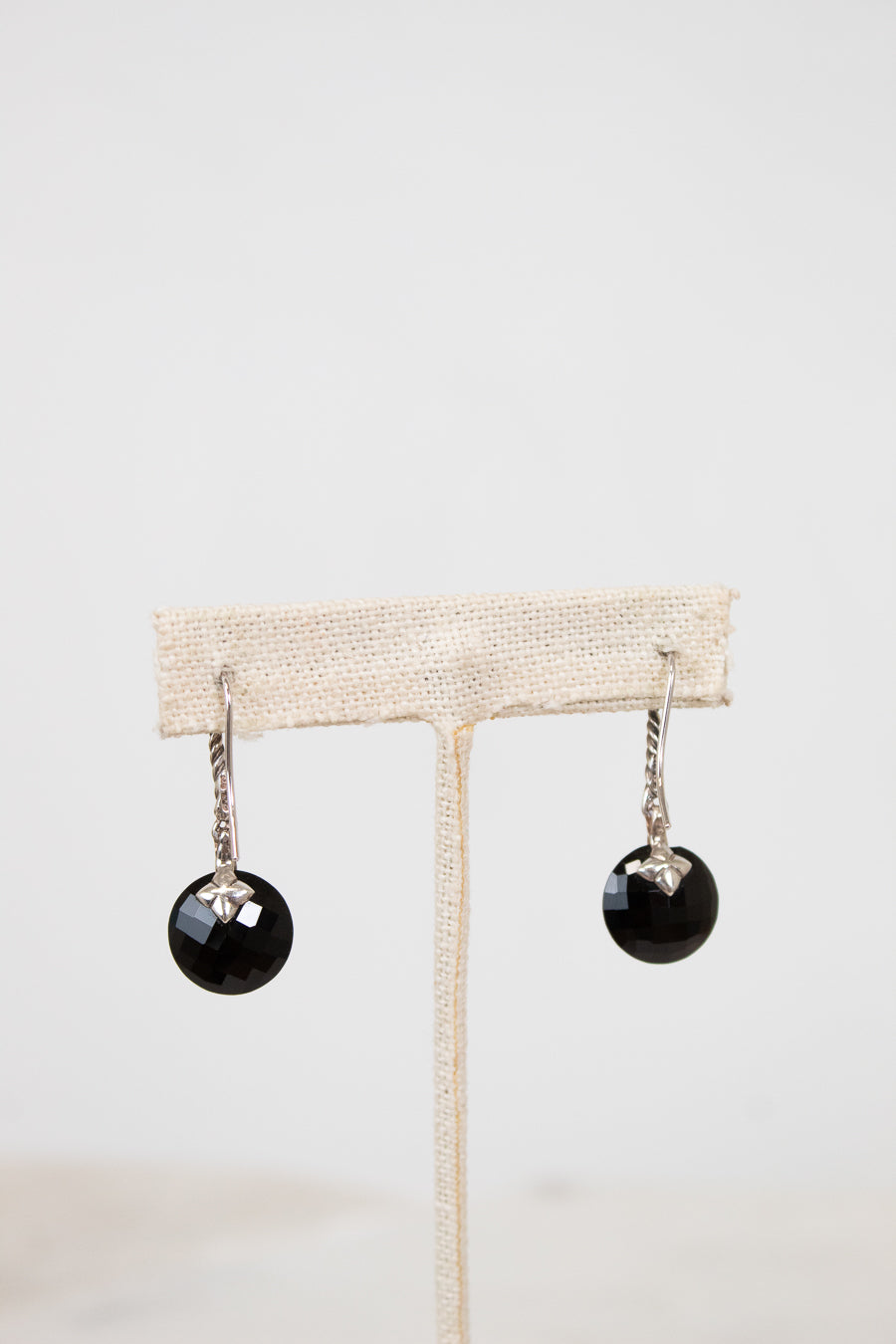 Black earrings on a beige earring stand against a white background