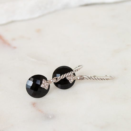 Pair of earrings with black gemstones and silver accents on a marble surface