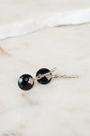 Pair of earrings with black gemstones and silver accents on a marble surface