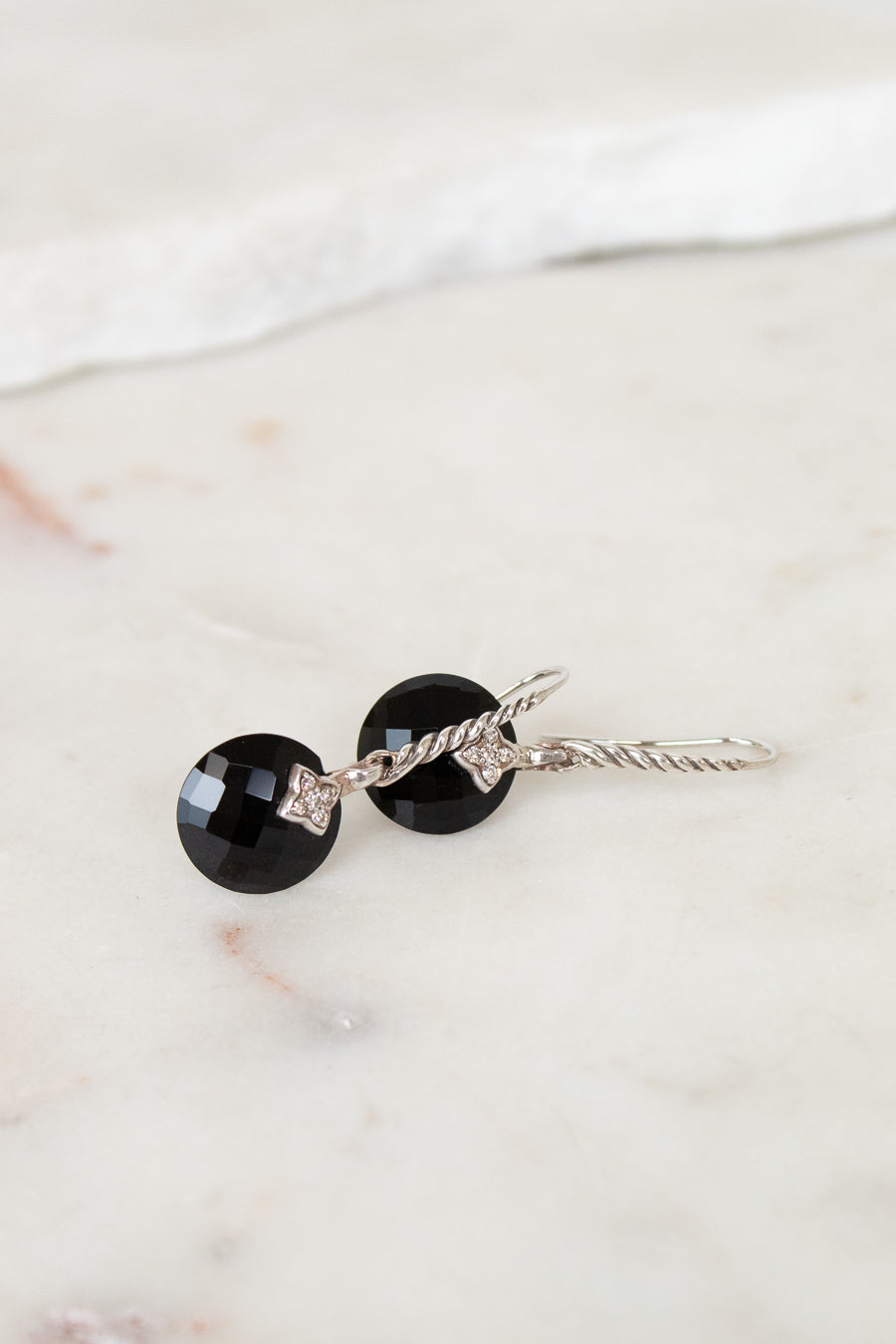 Pair of earrings with black gemstones and silver accents on a marble surface