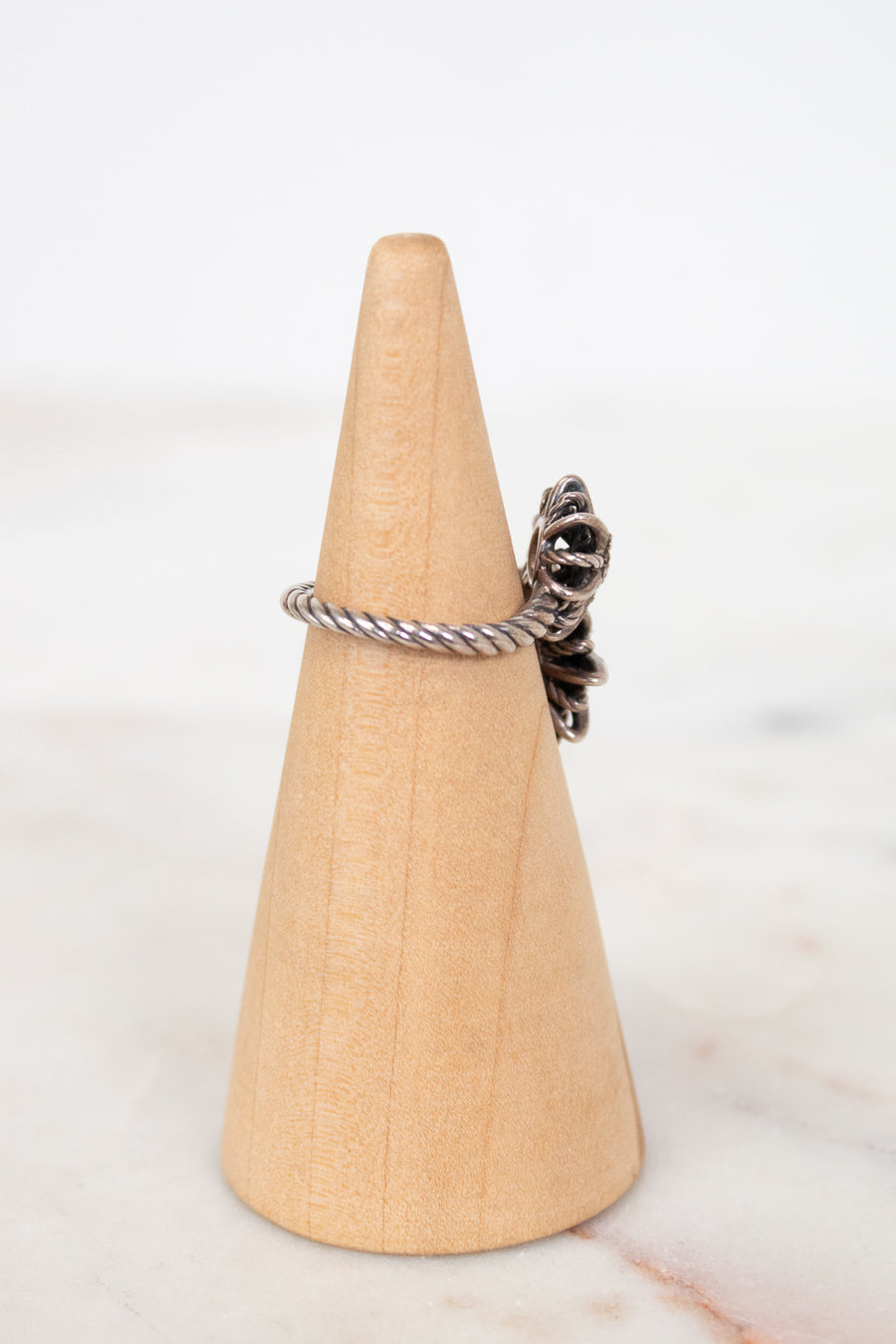 Silver ring with a unique design on a wooden cone against a white background