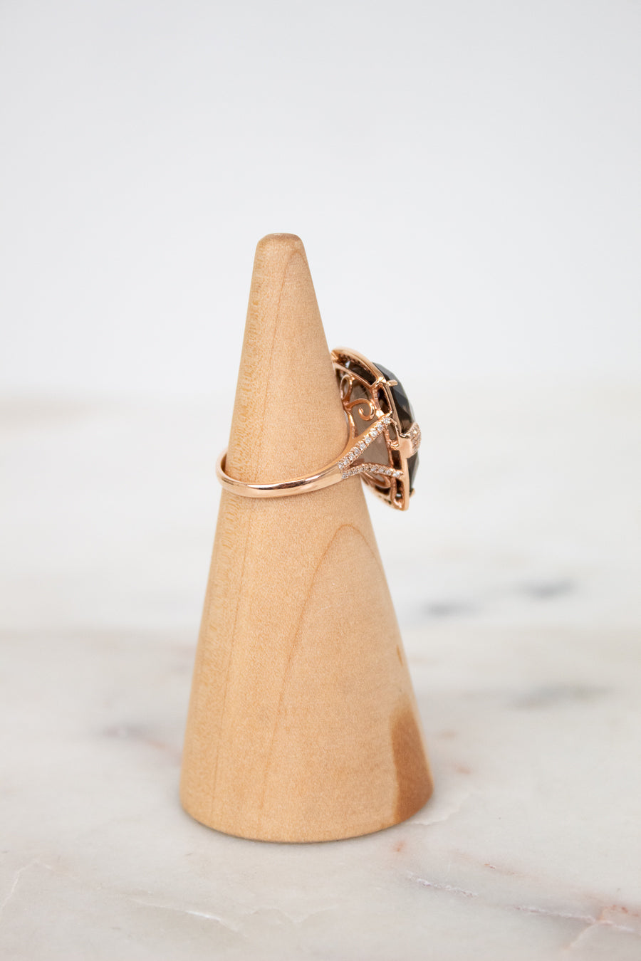 Wooden cone-shaped jewelry stand with a ring on a marble surface