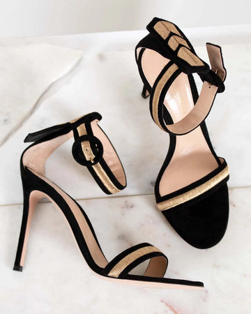 Black high-heeled sandals with gold strap detail on a light background