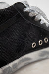 Close-up of a black sneaker with silver embellishments on a light background