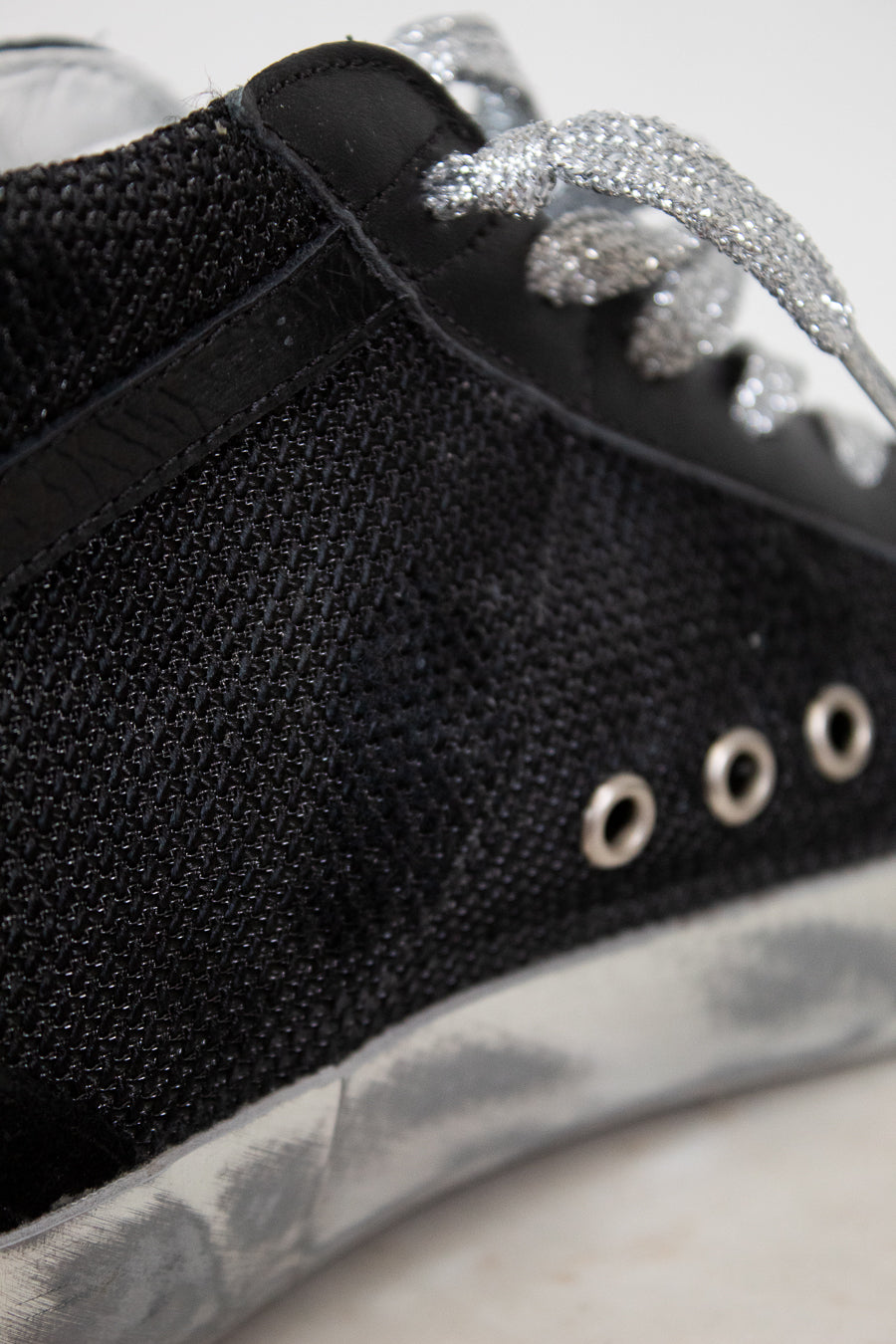 Close-up of a black sneaker with silver embellishments on a light background
