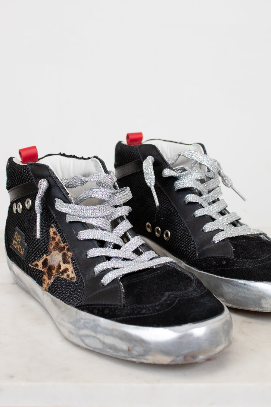 Black sneakers with white laces and a leopard print star on a light gray background
