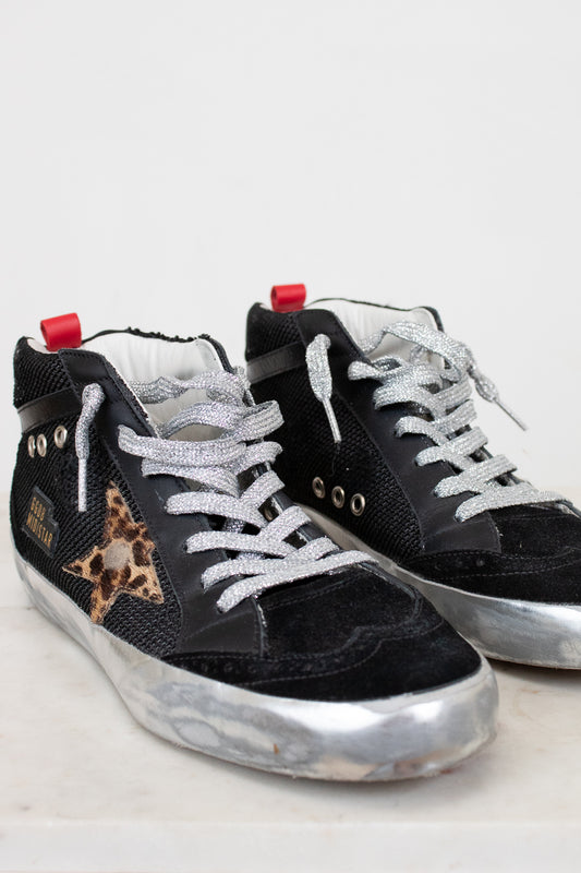 Black sneakers with white laces and a leopard print star on a light gray background