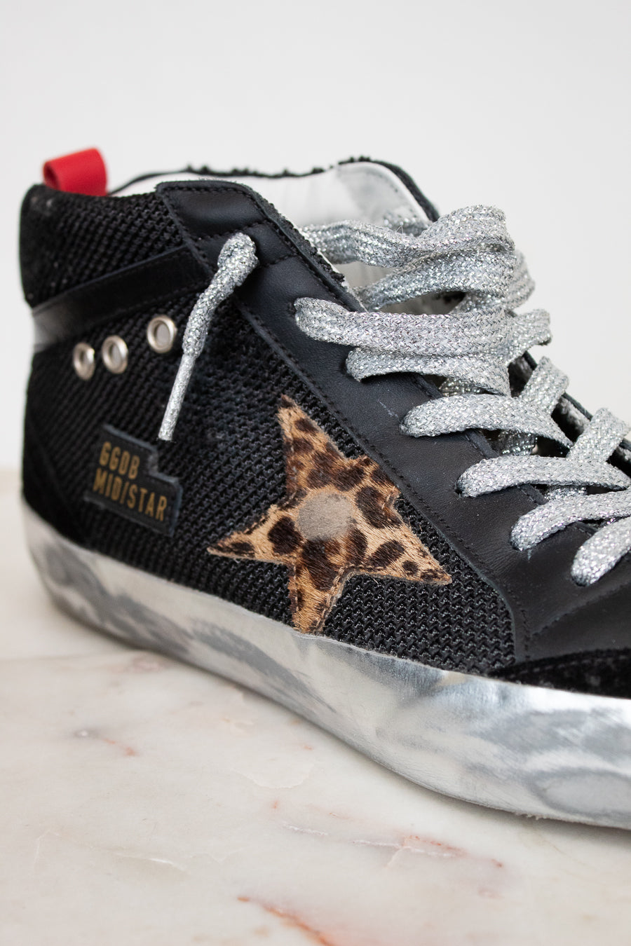 Black sneaker with silver laces and leopard print star on a marble surface