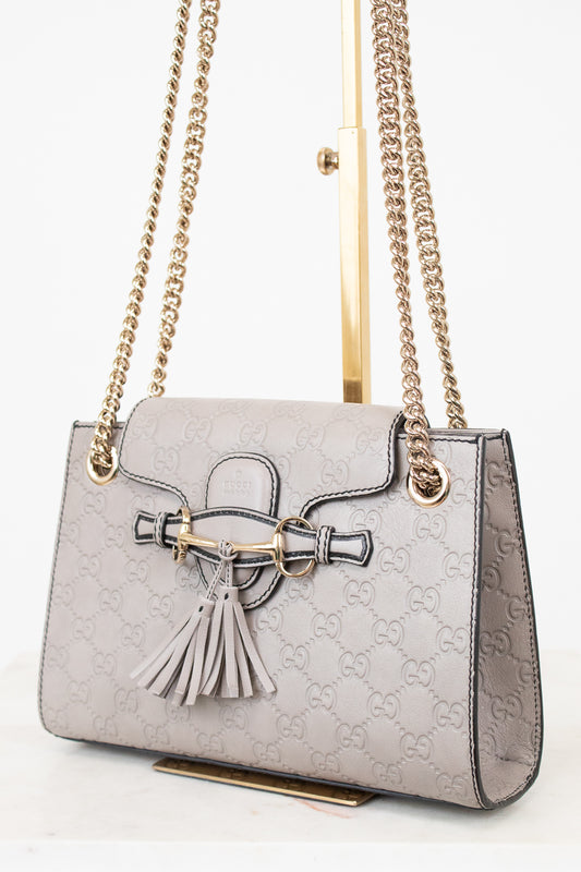 Grey handbag with chain strap and tassel on a white background
