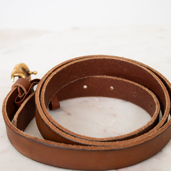 Brown leather belt with a gold buckle on a light marble background