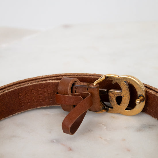 Brown leather belt with a gold buckle on a marble surface