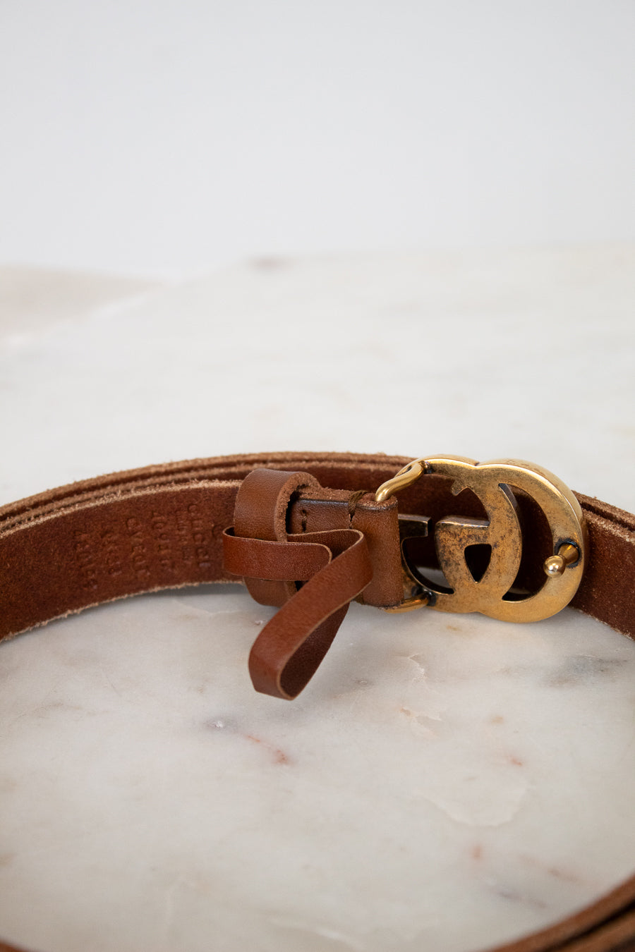 Brown leather belt with a gold buckle on a marble surface