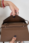 Brown handbag held by a hand with manicured nails against a neutral background