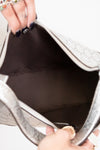 Close-up of a hand holding an open silver clutch bag with a brown interior.