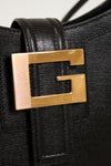 Black textured handbag with a gold logo on a light gray background