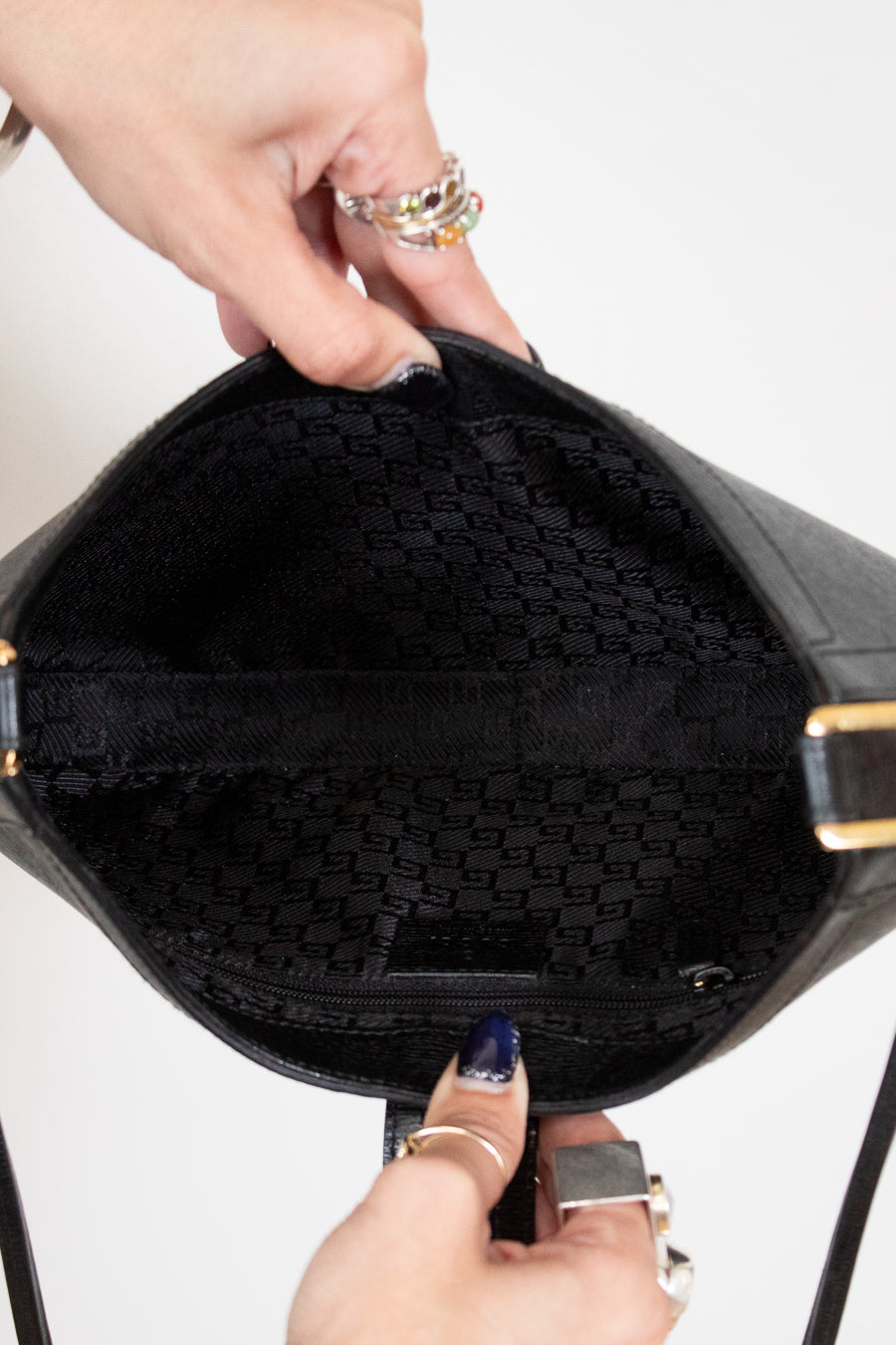 Black handbag with gold accents held open by a hand against a white background