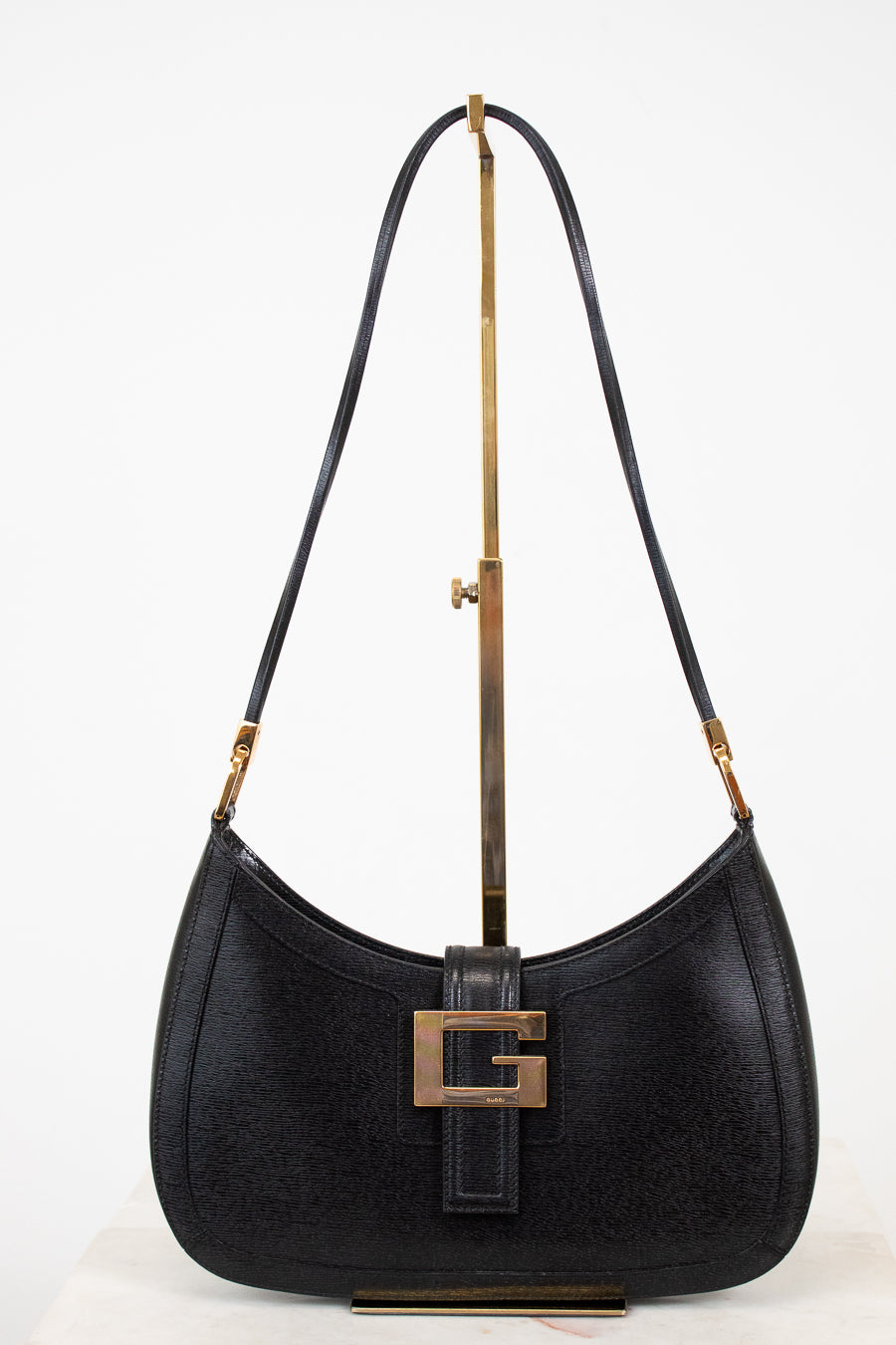 Black shoulder bag on gold stand with white background
