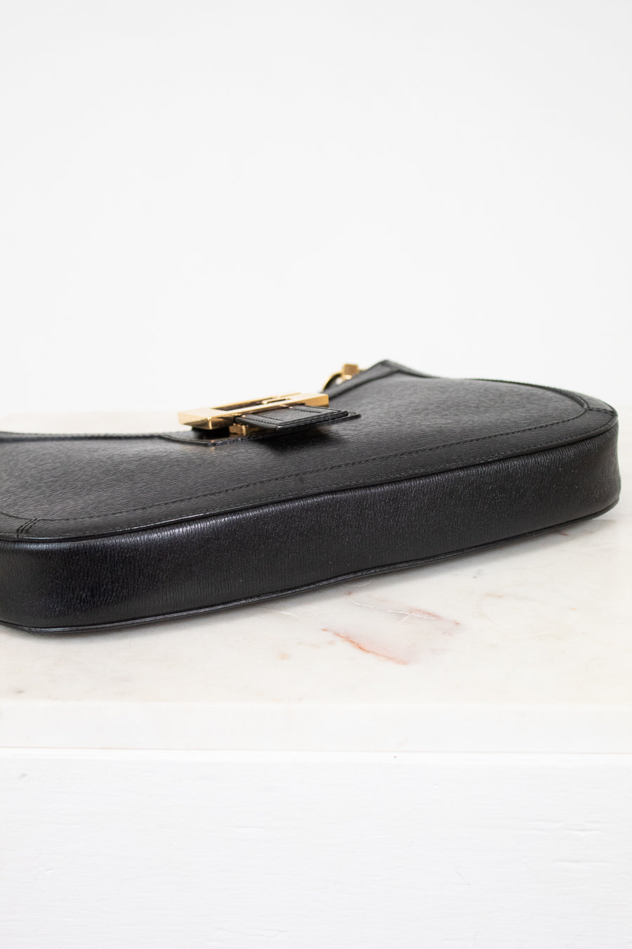 Black leather handbag with gold clasp on a light background