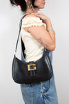 Person wearing overalls holding black shoulder bag with a white background