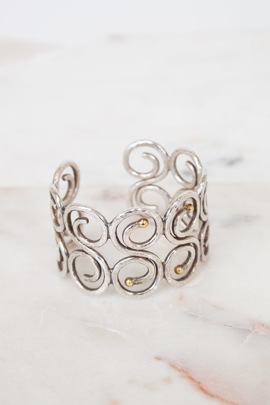 Silver cuff bracelet with intricate designs on a marble surface