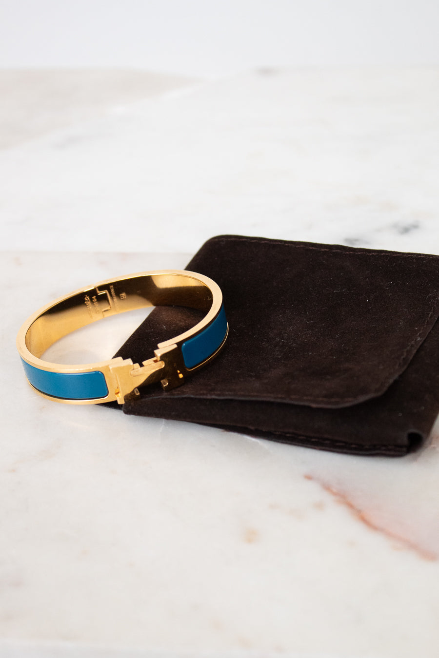 Gold and blue bracelet on a black pouch against a marble background
