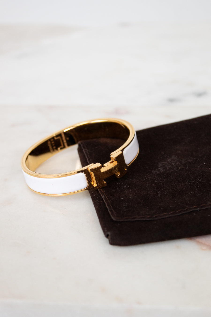 Gold and white bracelet on a black jewelry pouch with a marble background