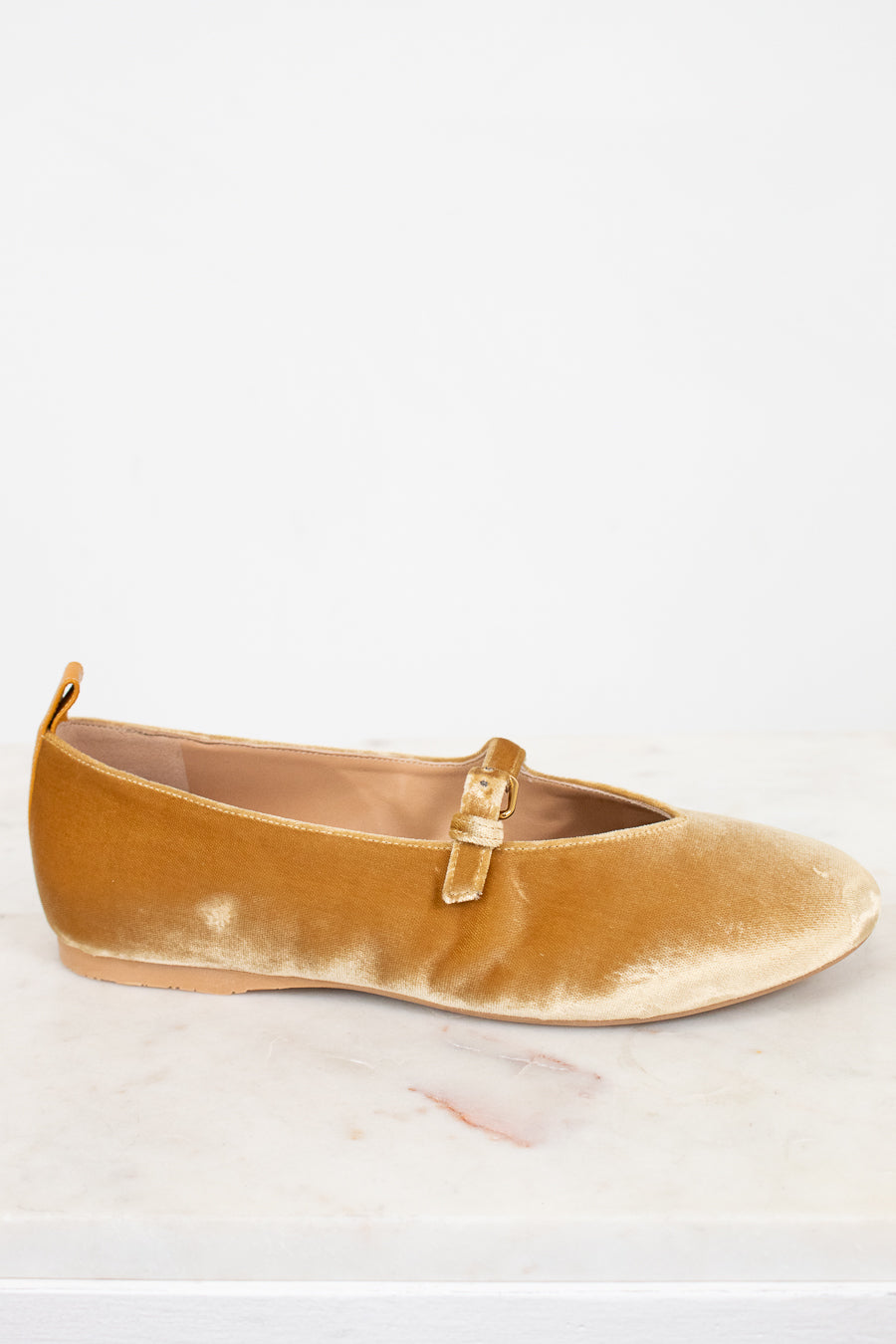 Gold velvet flat shoe with a gold buckle on a light gray background