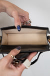 Close-up of a hand holding an open black handbag with beige interior.
