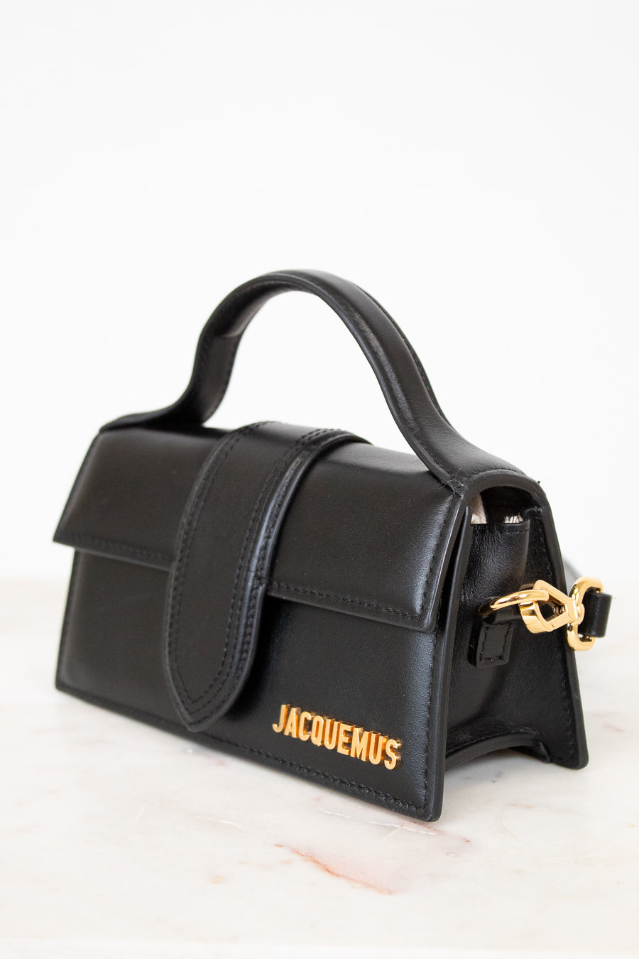 Black handbag with gold clasp and 'Jacquemus' branding on a white background