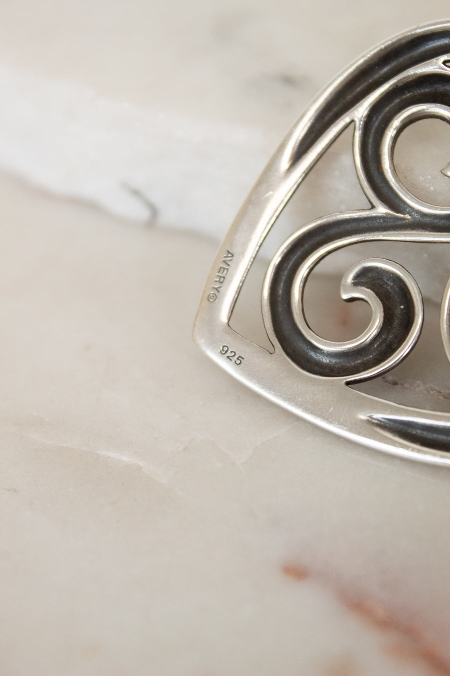 Silver pendant with intricate design on a marble surface