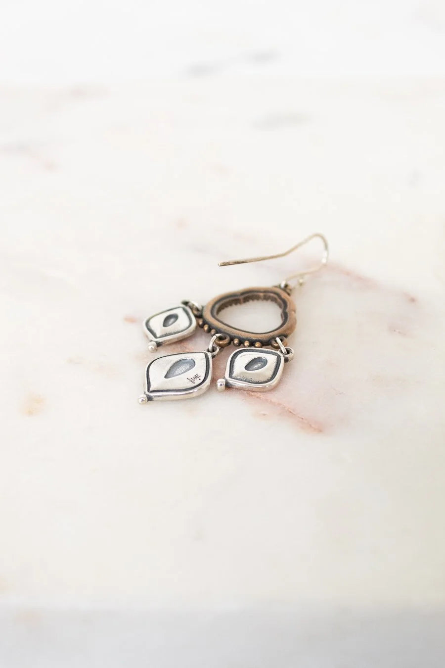 Pair of silver earrings with teardrop-shaped charms on a marble surface