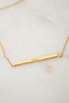 Gold necklace with a bar pendant on a light background