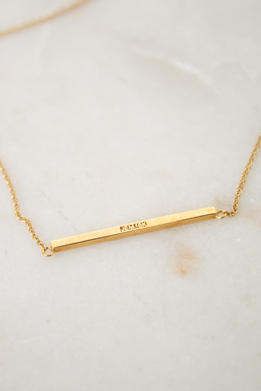 Gold necklace with a bar pendant on a light background