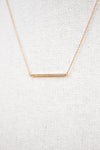 Gold necklace with a bar pendant on a light gray textured background