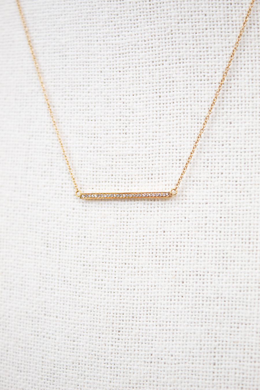 Gold necklace with a bar pendant on a light gray textured background