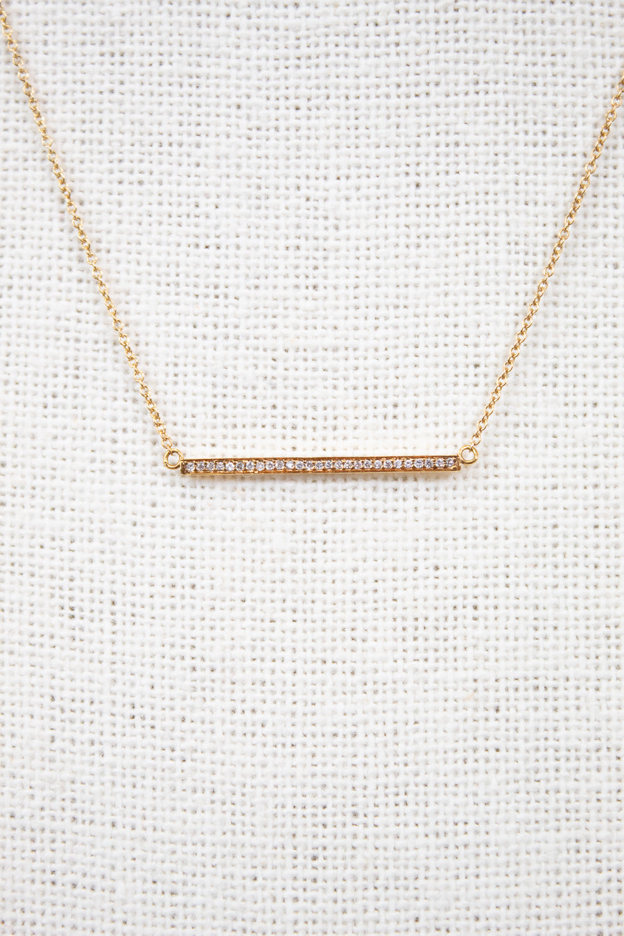 Gold necklace with a bar pendant on a light gray background
