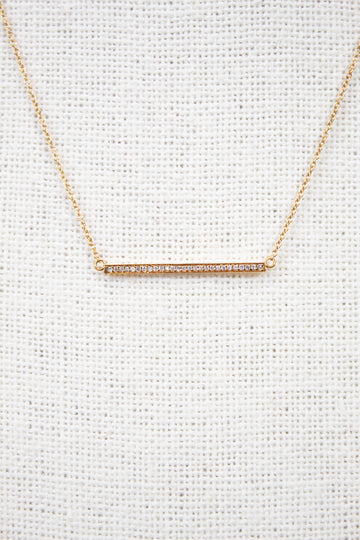 Gold necklace with a bar pendant on a light gray background