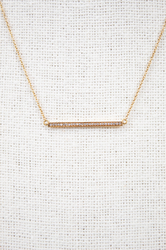 Gold necklace with a bar pendant on a light gray background