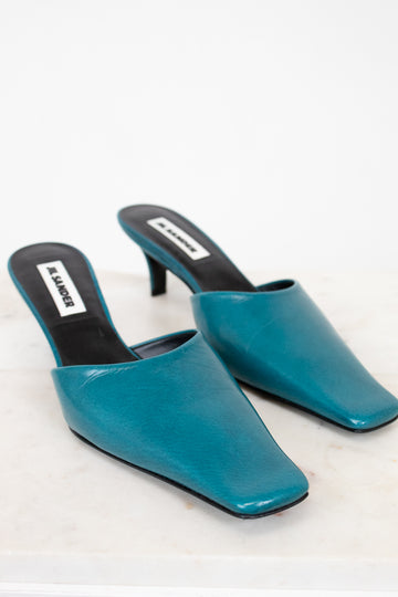 Pair of teal high-heeled mules on a white background