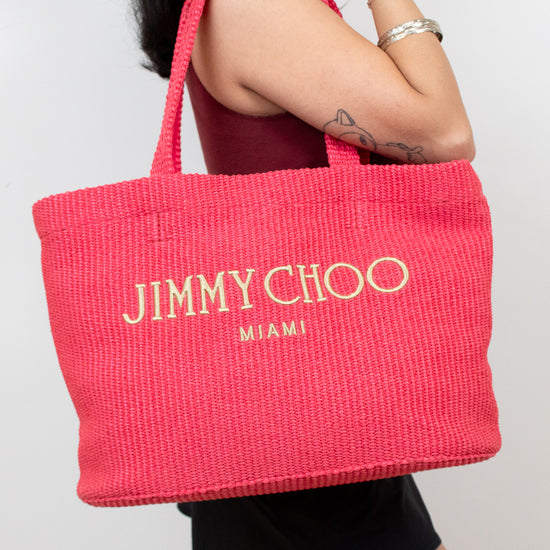 Person holding a pink tote bag with 'Jimmy Choo Miami' branding.