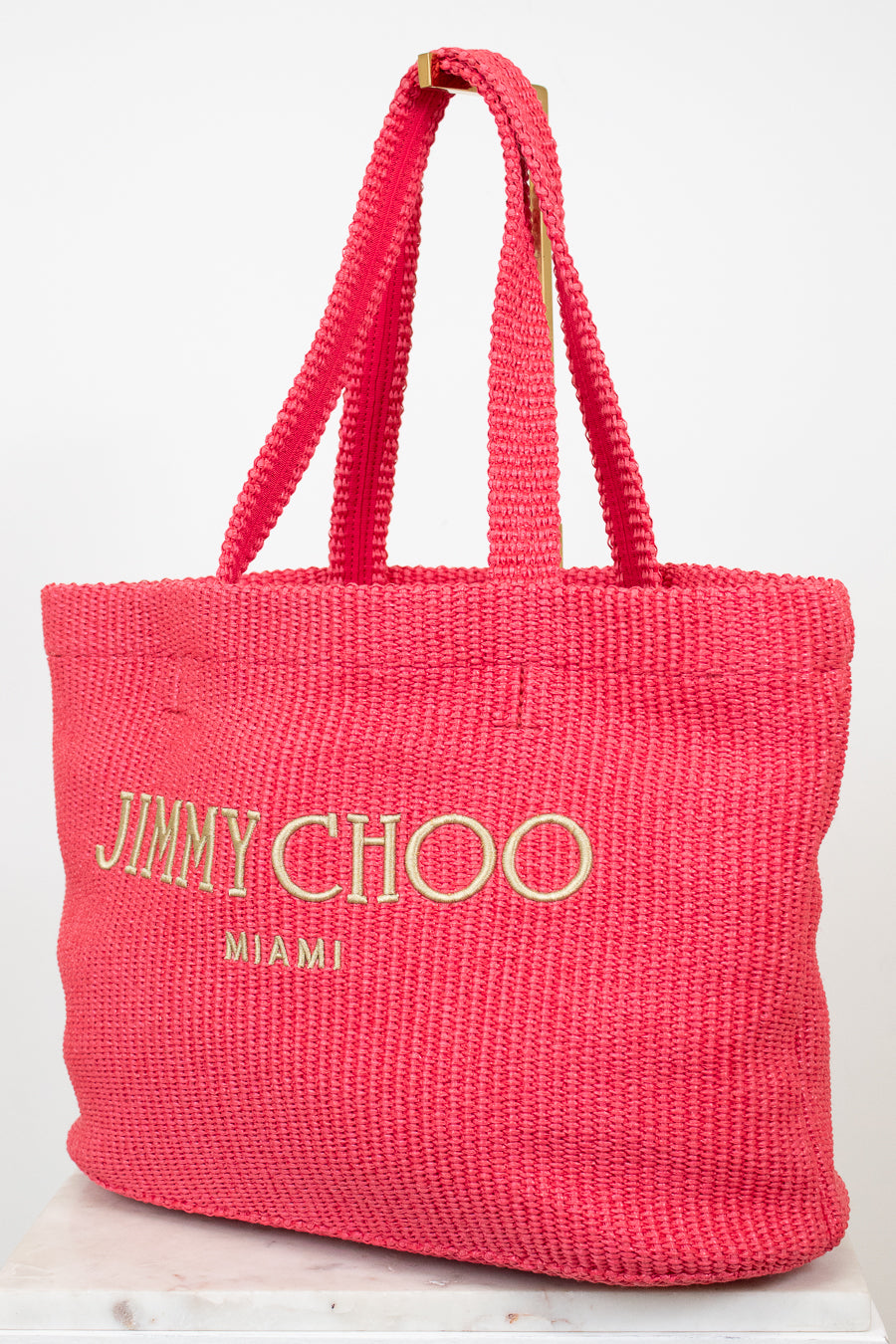 Pink woven handbag with 'Jimmy Choo Miami' text on a white background