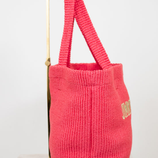 Pink woven bag with gold text on a white background