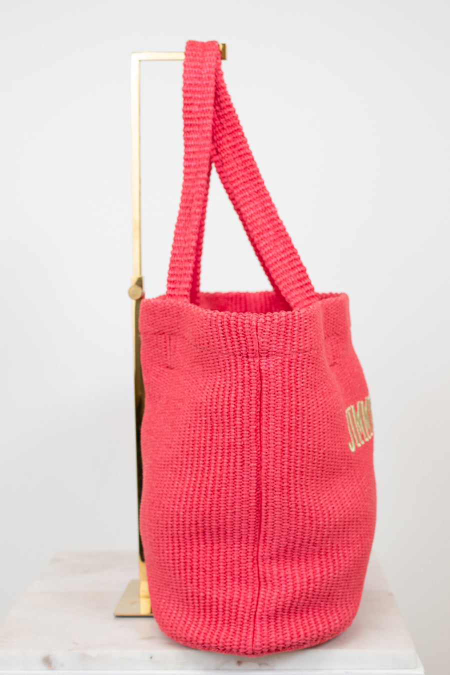 Pink woven bag with gold text on a white background