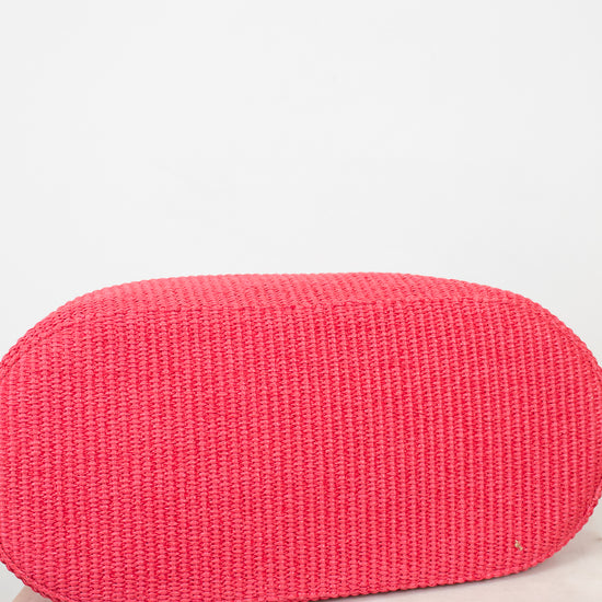 Red woven clutch bag on a light wooden surface with a white background