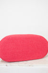 Red woven clutch bag on a light wooden surface with a white background