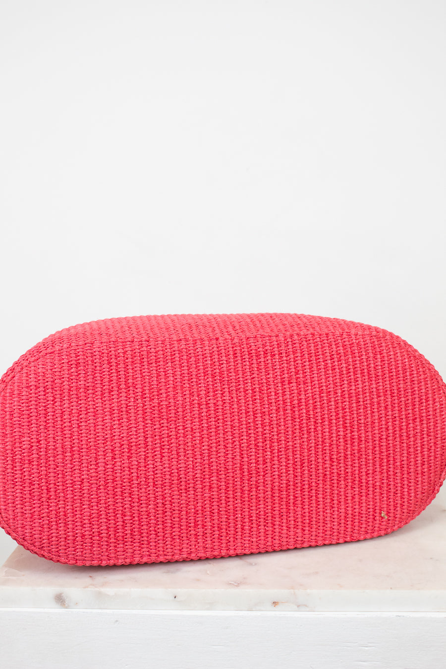 Red woven clutch bag on a light wooden surface with a white background