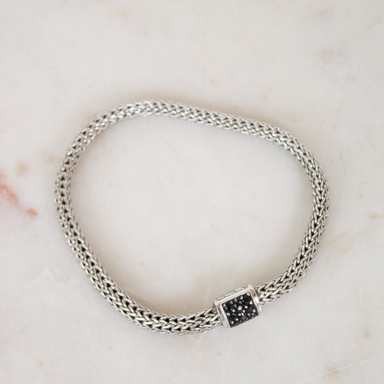 Silver braided bracelet with small black sapphires on a white marble background