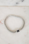 Silver braided bracelet with small black sapphires on a white marble background
