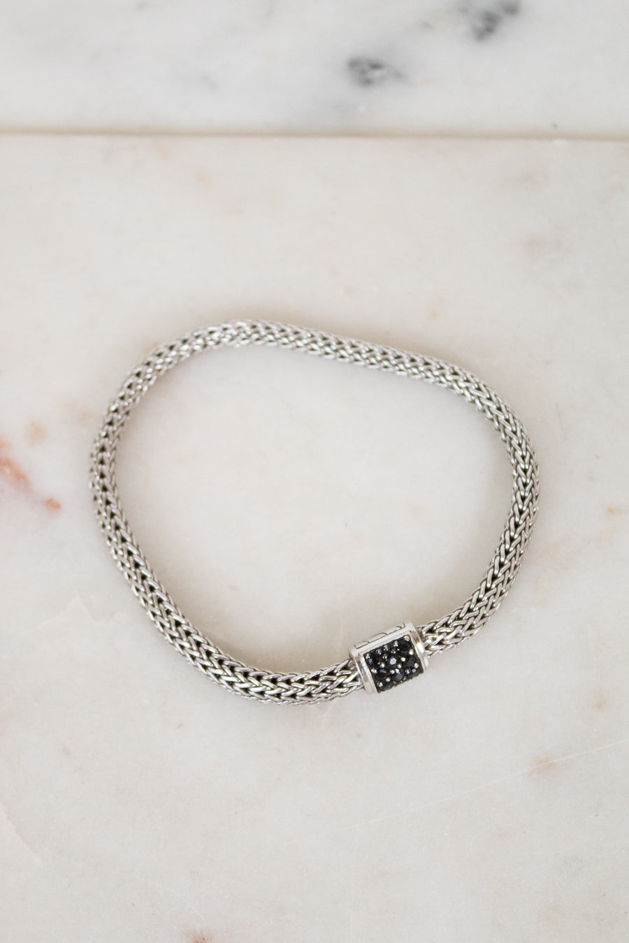 Silver braided bracelet with small black sapphires on a white marble background