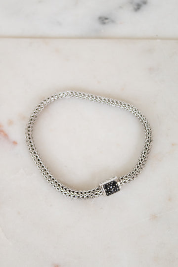 Silver braided bracelet with small black sapphires on a white marble background